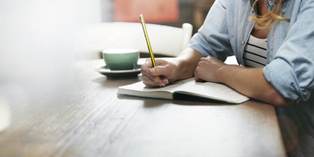 Woman writing in her notebook. Cup of coffee on her desk