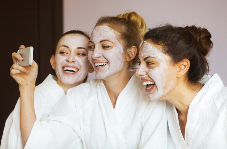 3 glückliche Kundinnen in einem Kosmetikinstitut. Sie haben Gesichtsmasken und machen ein Selfie.